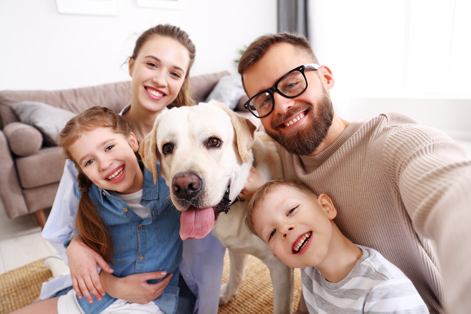 Laughing family with kids and dog hugging at home